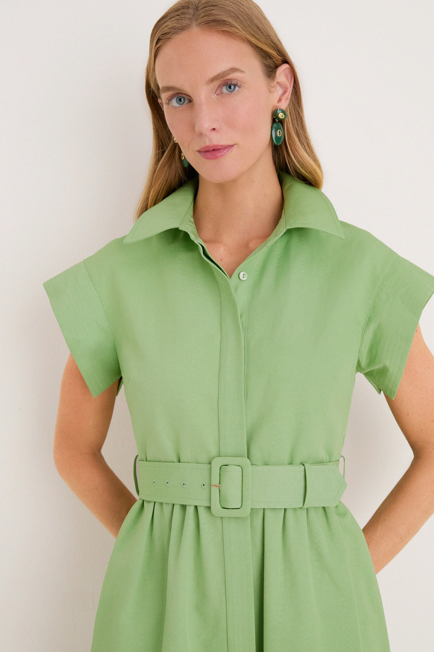 Woman wearing the classic Pistachio Chloe Dress, a high-end, effortless shirtdress with a belt, pointed collar, and concealed placket, paired with green-accented drop earrings.