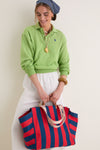 Person holding the classic Poppy and French Blue Beach Tote, styled with an effortless, high-end, summery outfit featuring a headscarf, necklaces, and a wooden bangle.