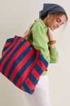 Woman in green top carrying a classic, high-end Poppy and French Blue Beach Tote, showcasing its effortless, fun style with leather handles and a webbed shoulder strap.