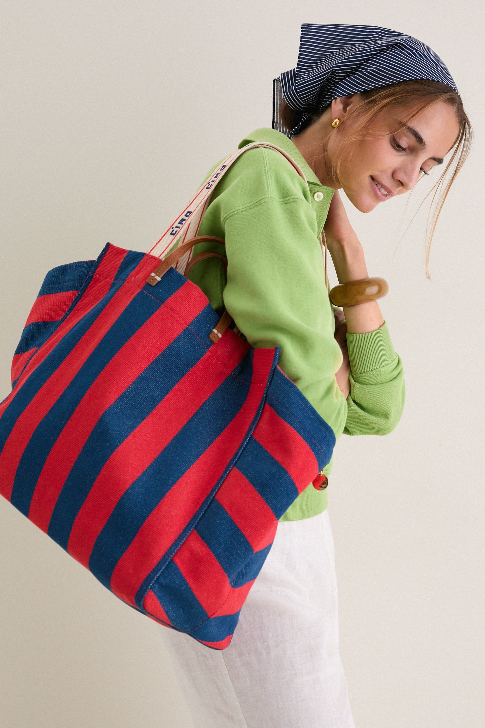Woman in green top carrying a classic, high-end Poppy and French Blue Beach Tote, showcasing its effortless, fun style with leather handles and a webbed shoulder strap.