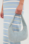 Person holding the Baby Blue Gnocchi Bag, a classic, crescent-shaped suede hobo with zip closure, effortlessly complementing a form-fitting, striped dress for a fun, high-end look.
