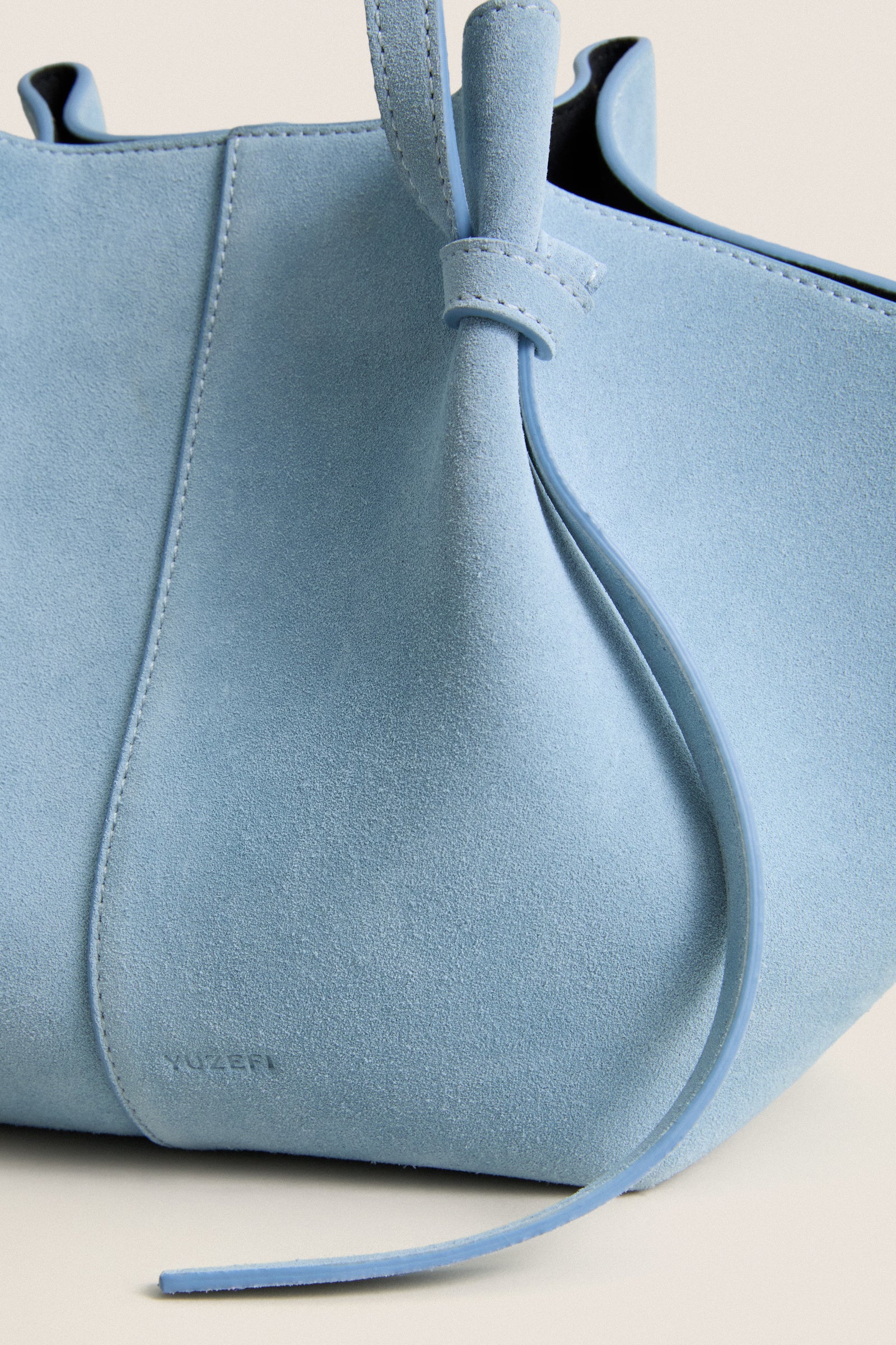 Ocean Mochi Suede Bag close-up: classic light blue suede, stitched panels, thin suede strap, knotted detail. Effortless, high-end design for fun, everyday use.