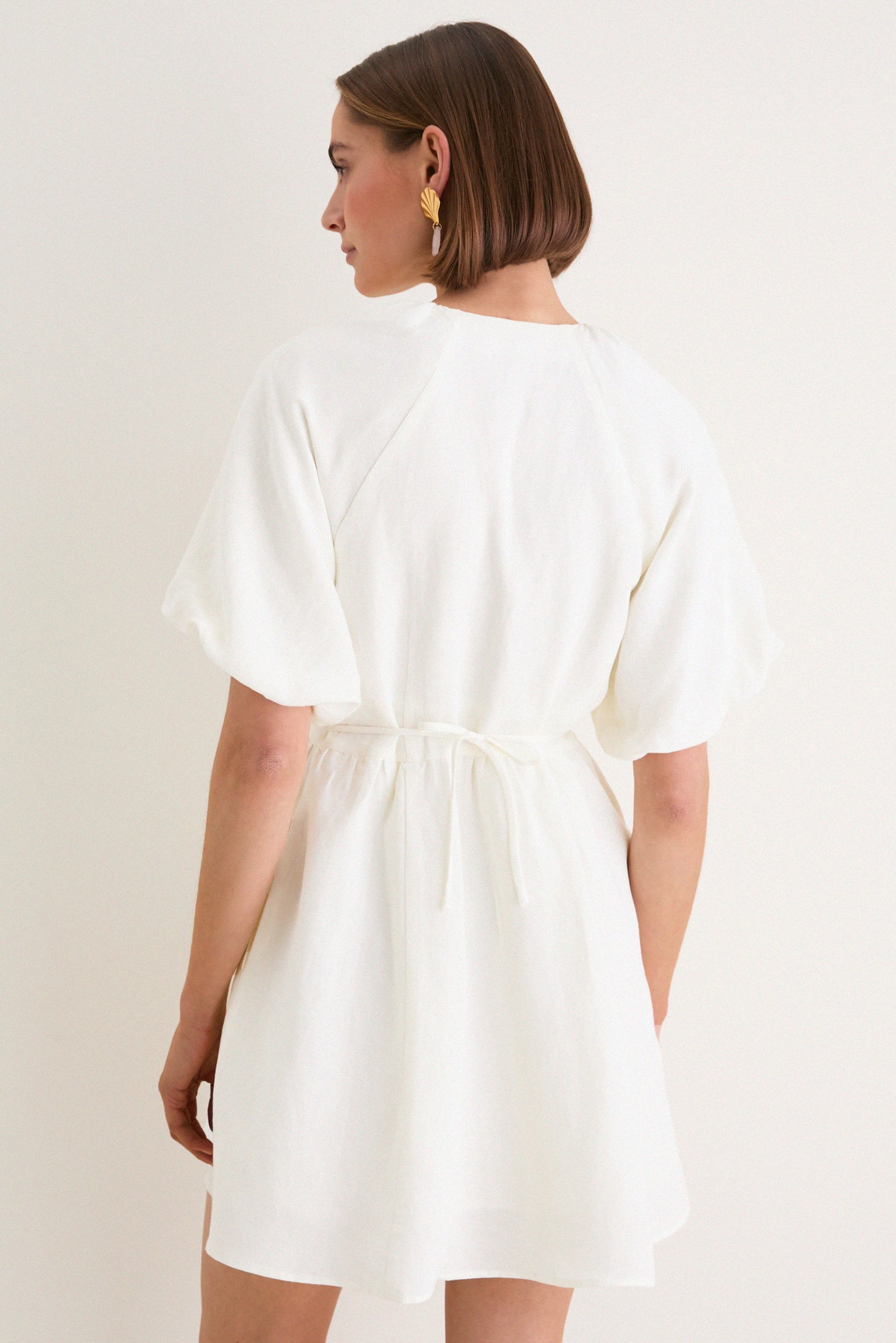 Woman in an off-white Star White Bastille Short Dress with puffed sleeves and cinched waist, embodying a classic, effortless style with high-end, fun details.
