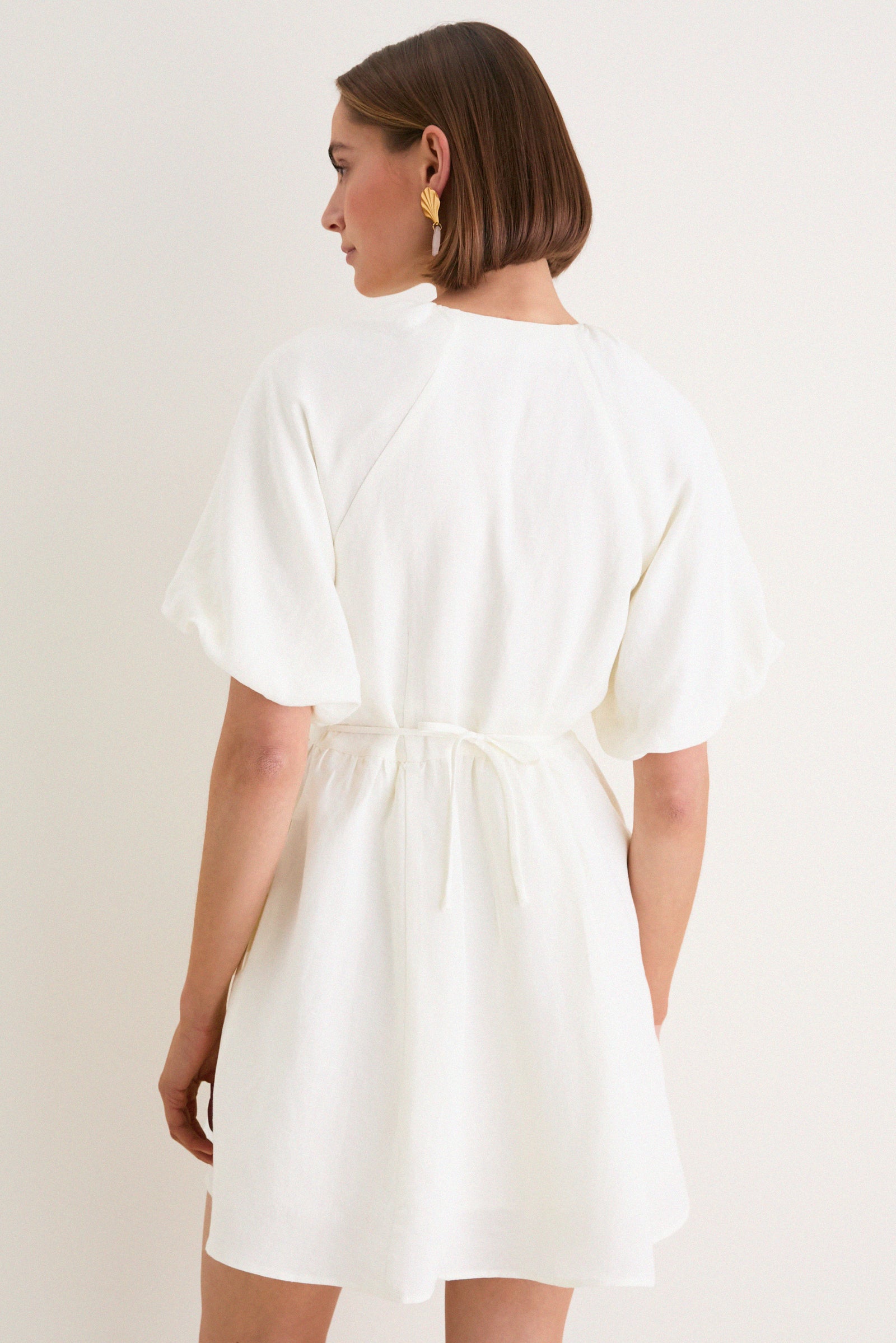 Woman in an off-white Star White Bastille Short Dress with puffed sleeves and cinched waist, embodying a classic, effortless style with high-end, fun details.