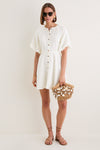 Woman wearing the classic Star White Bastille Short Dress, with effortless puffed sleeves and a button-front, accessorized with a woven straw tote, embodying high-end, fun style.
