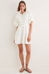 Model in classic, white Star White Bastille Short Dress with flutter sleeves, high neckline, self-tie waist, paired with tan sandals and statement earrings. Effortless, high-end style.