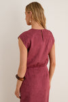 Back view of a woman in a classic, sleeveless Fig Gisella Top, showcasing its crinkled texture and elasticized waist. The look is effortlessly high-end with fun accessories.