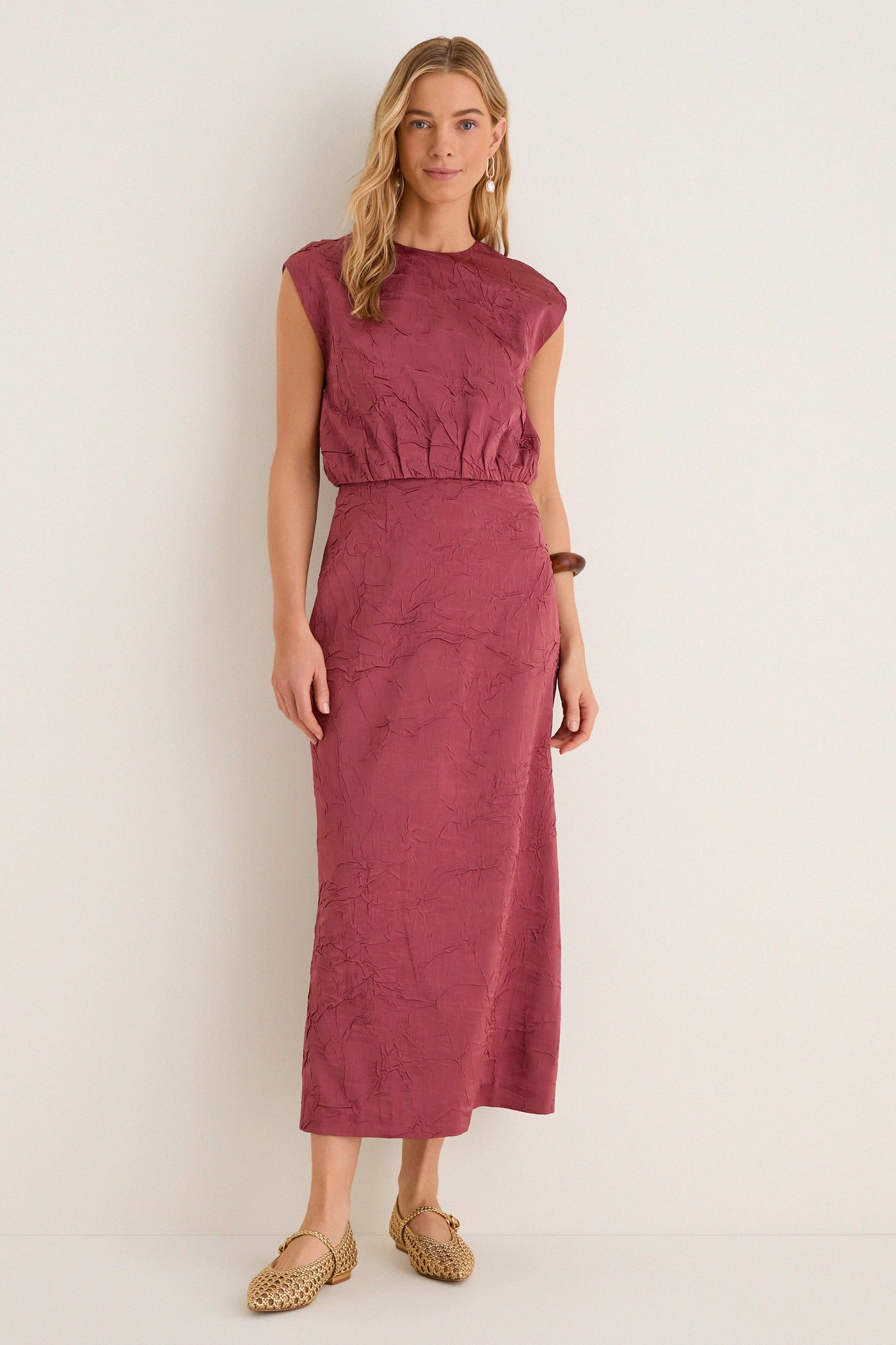 Woman in classic, sleeveless Fig Gisella Top, crinkled satin, paired with matching skirt. Effortless, high-end style: woven gold flats, wooden bangle, drop earrings.