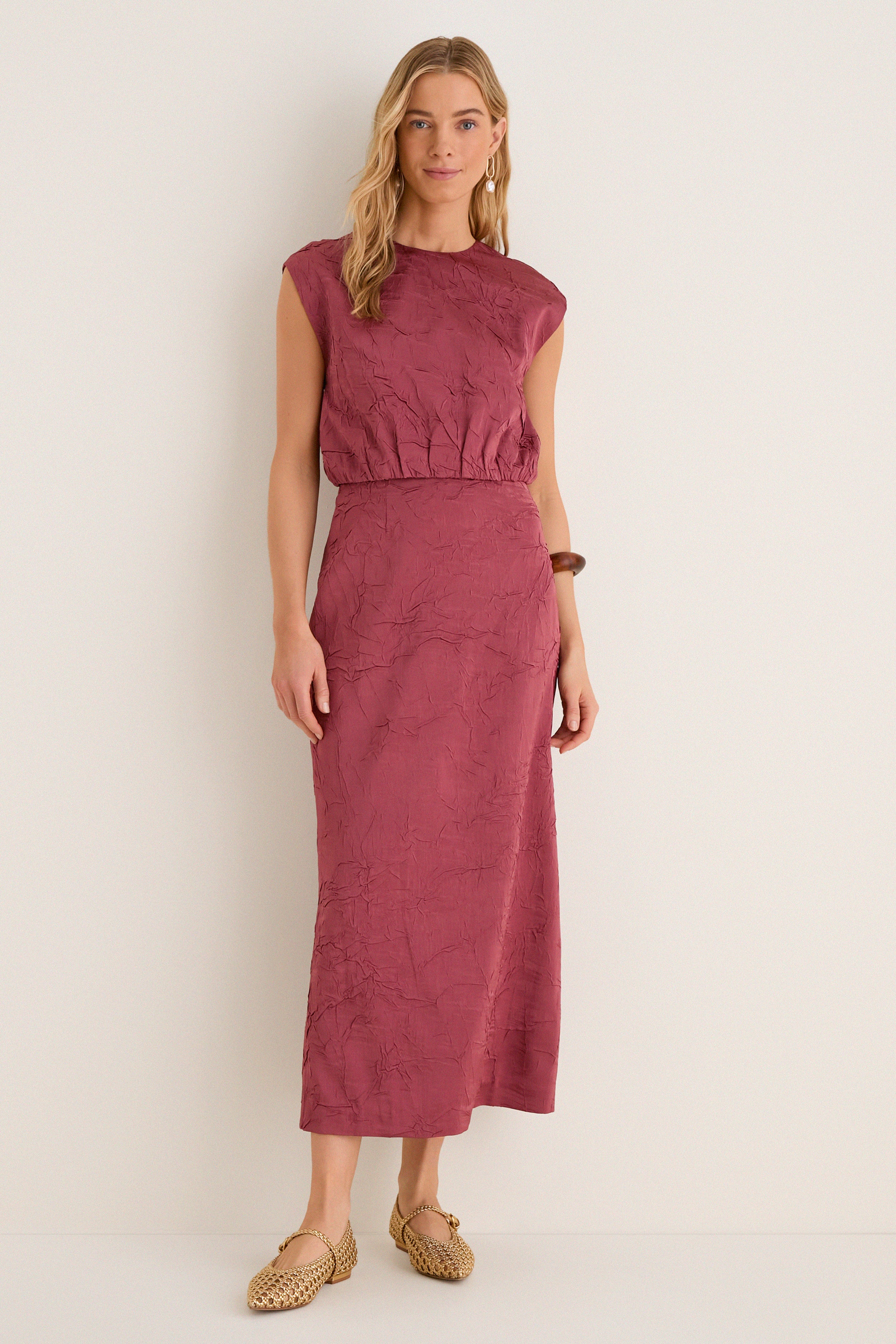 Woman in classic, sleeveless Fig Gisella Top, crinkled satin, paired with matching skirt. Effortless, high-end style: woven gold flats, wooden bangle, drop earrings.
