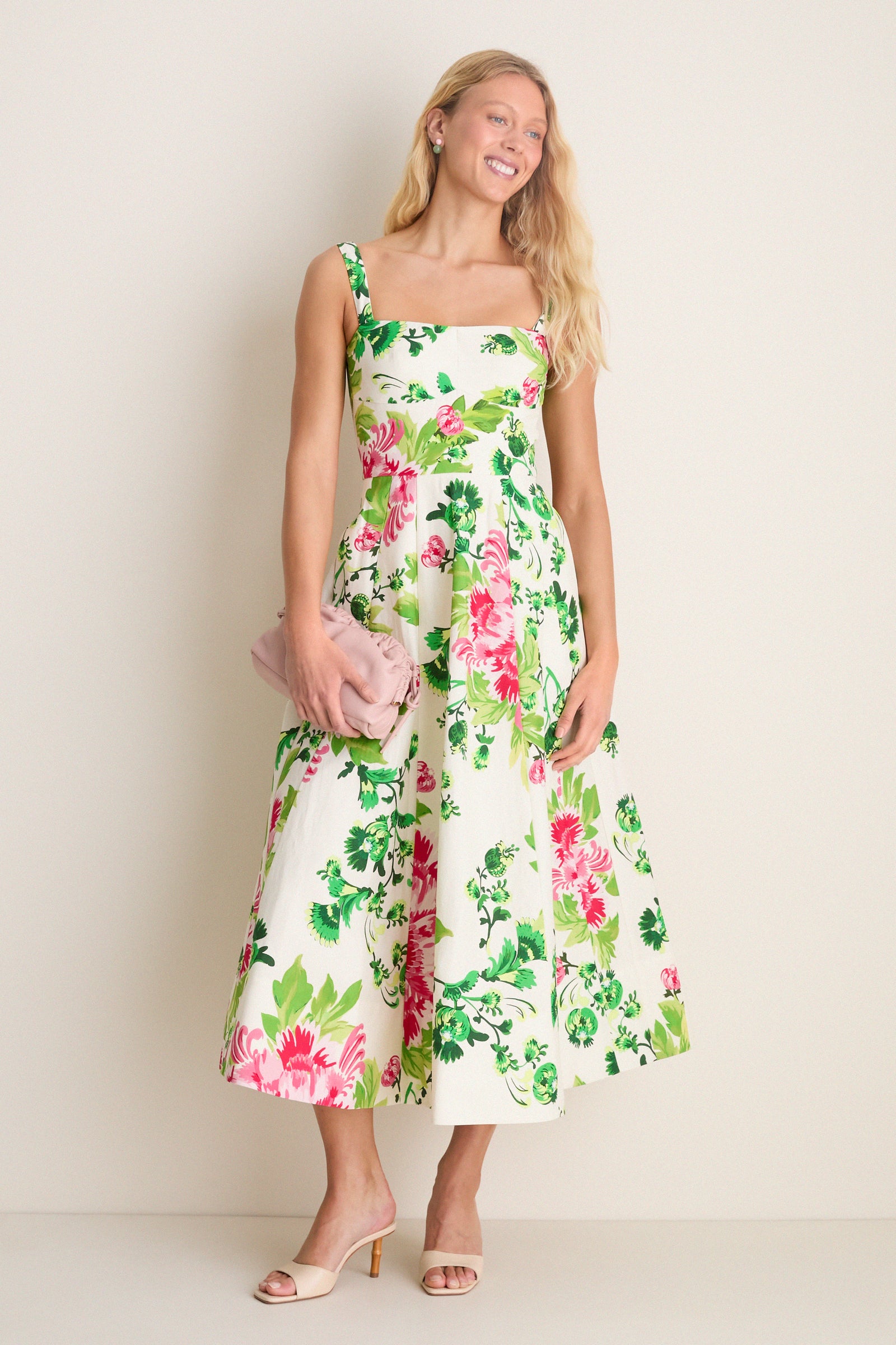 Saffier Bouquet Sabrina Midi Dress: A classic, effortless midi with bold floral print, square neckline, and flared skirt. Paired with a pink clutch and nude heeled mules.