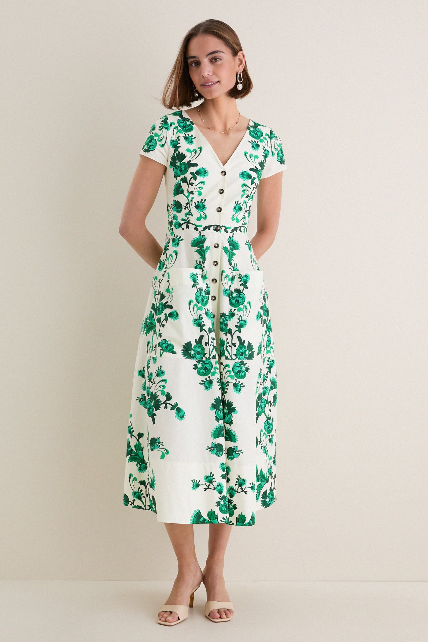 Woman in a classic Saffier Vines Zoey-E Midi Dress, featuring effortless green floral print, V-neck, button-front, and patch pockets; paired with open-toe mules.