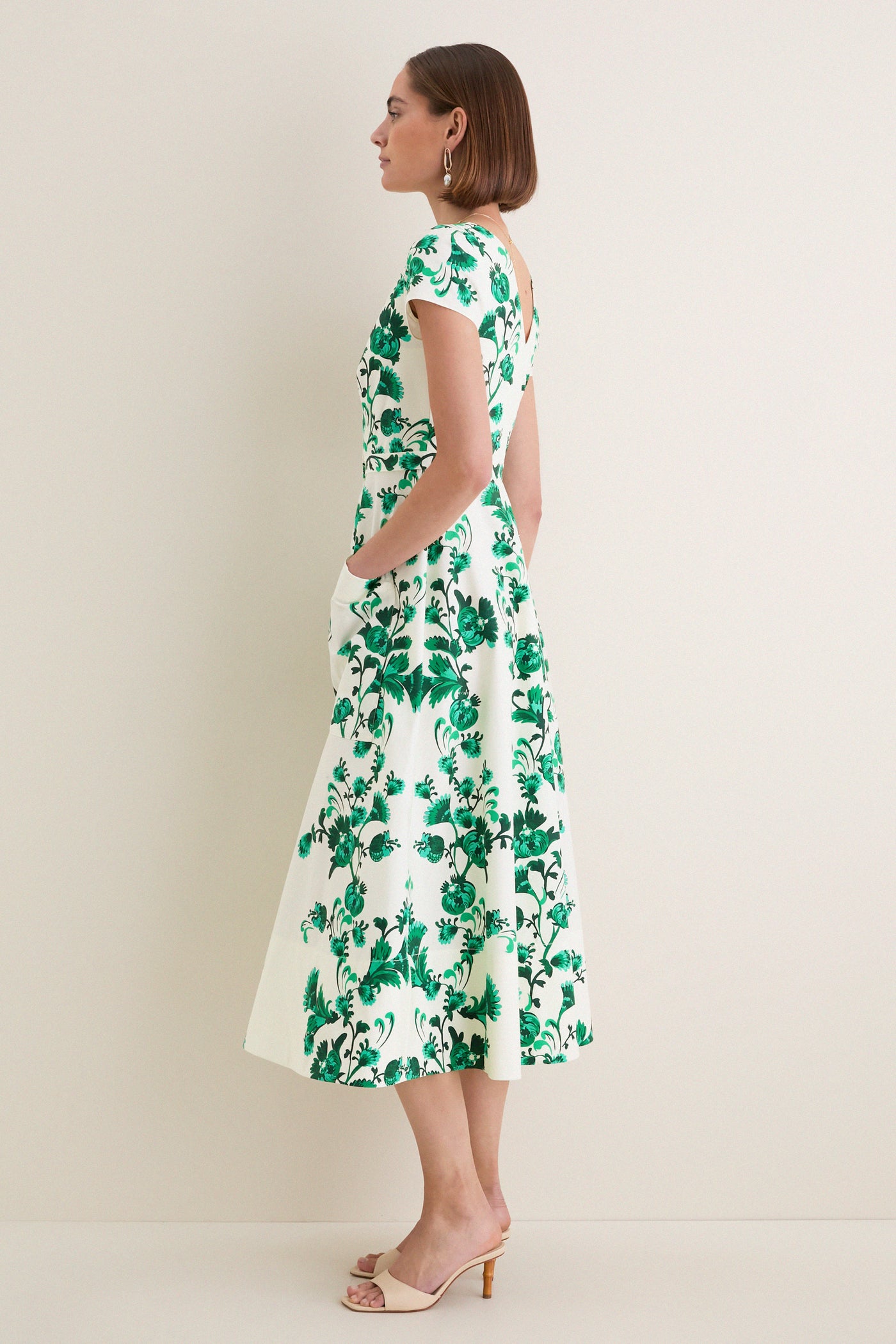 Woman in profile wearing the classic Saffier Vines Zoey-E Midi Dress with green vine motifs, cap sleeves, and beige mule heels, exuding effortless, high-end elegance.