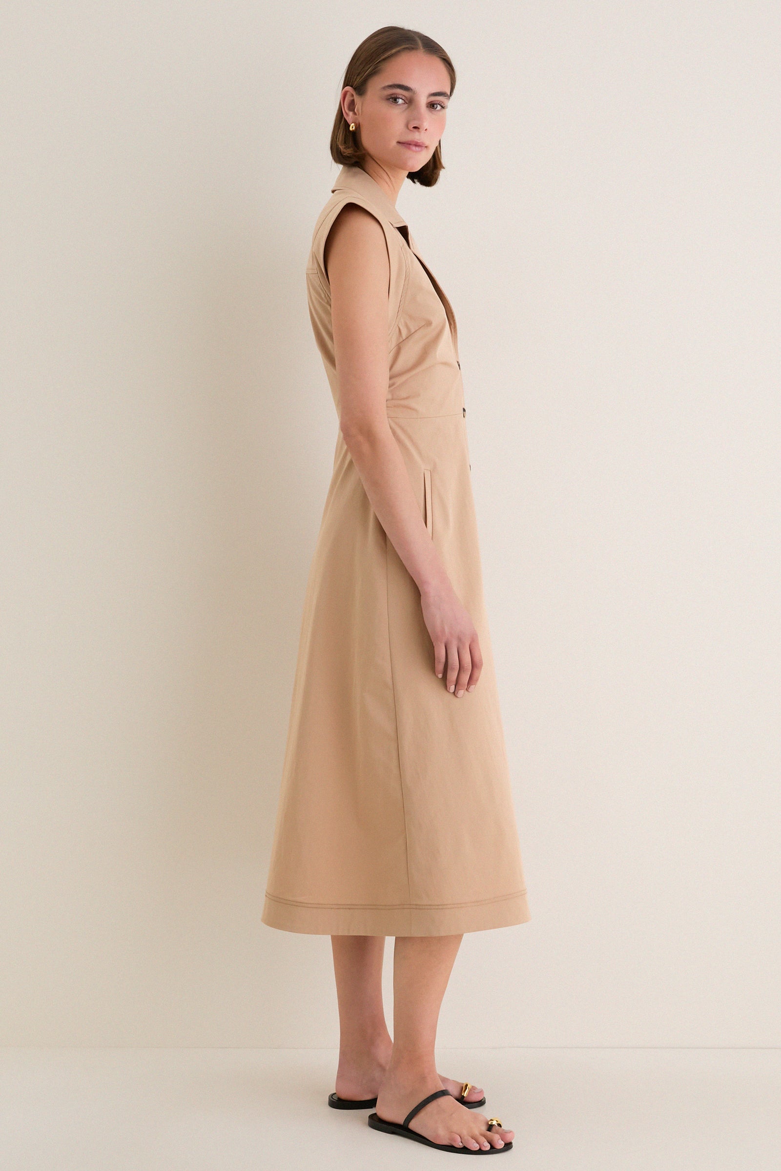 Young woman in profile wearing a classic Khaki Orla Dress with a modern notched collar, sleeveless design, and button-down front, paired with effortless black sandals.