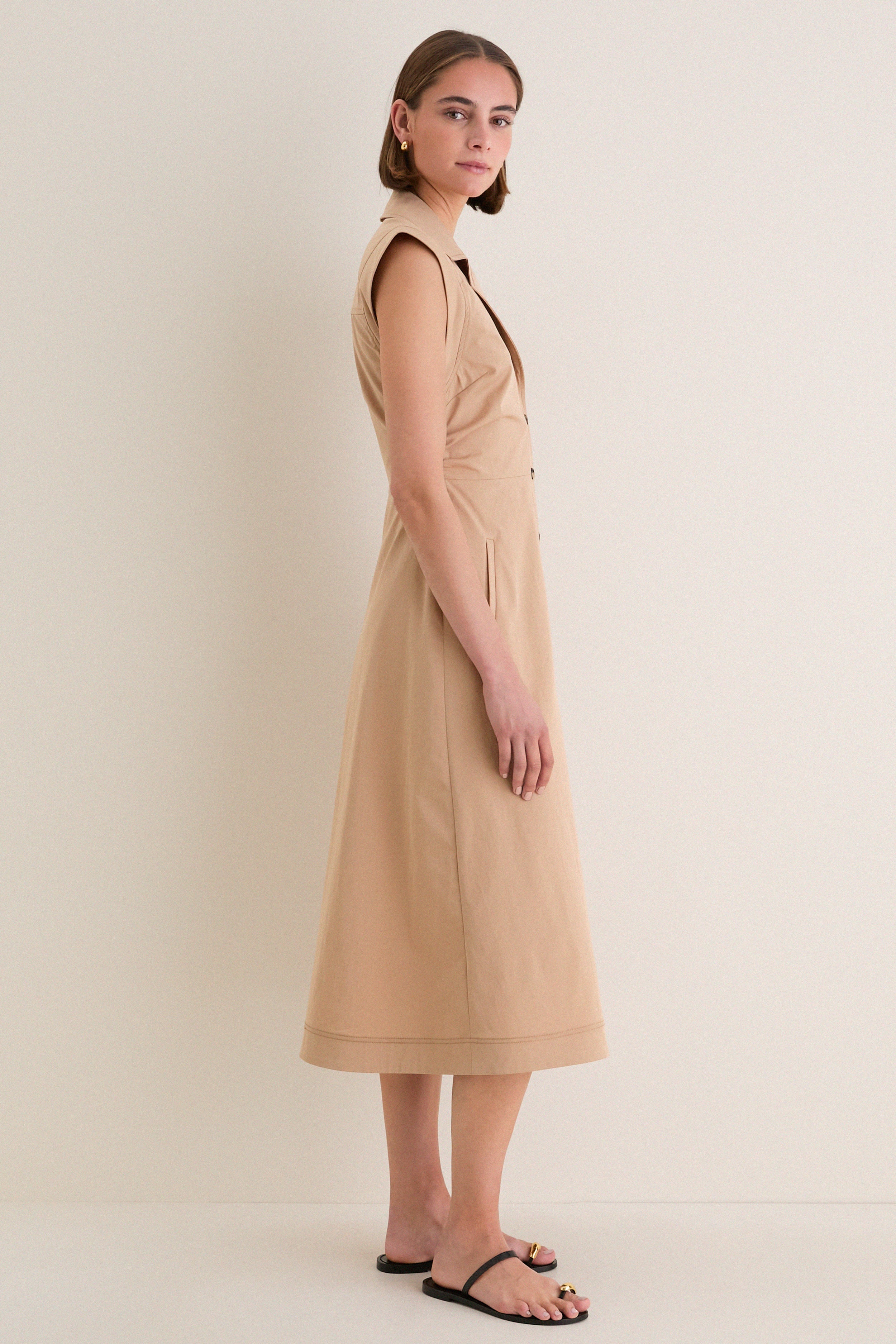 Young woman in profile wearing a classic Khaki Orla Dress with a modern notched collar, sleeveless design, and button-down front, paired with effortless black sandals.