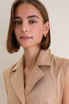 Young woman wearing the classic Khaki Orla Dress with gold hoop earrings, showcasing its effortless fit-and-flare design, cap sleeves, and tailored detailing. High-end, fun, and versatile style.
