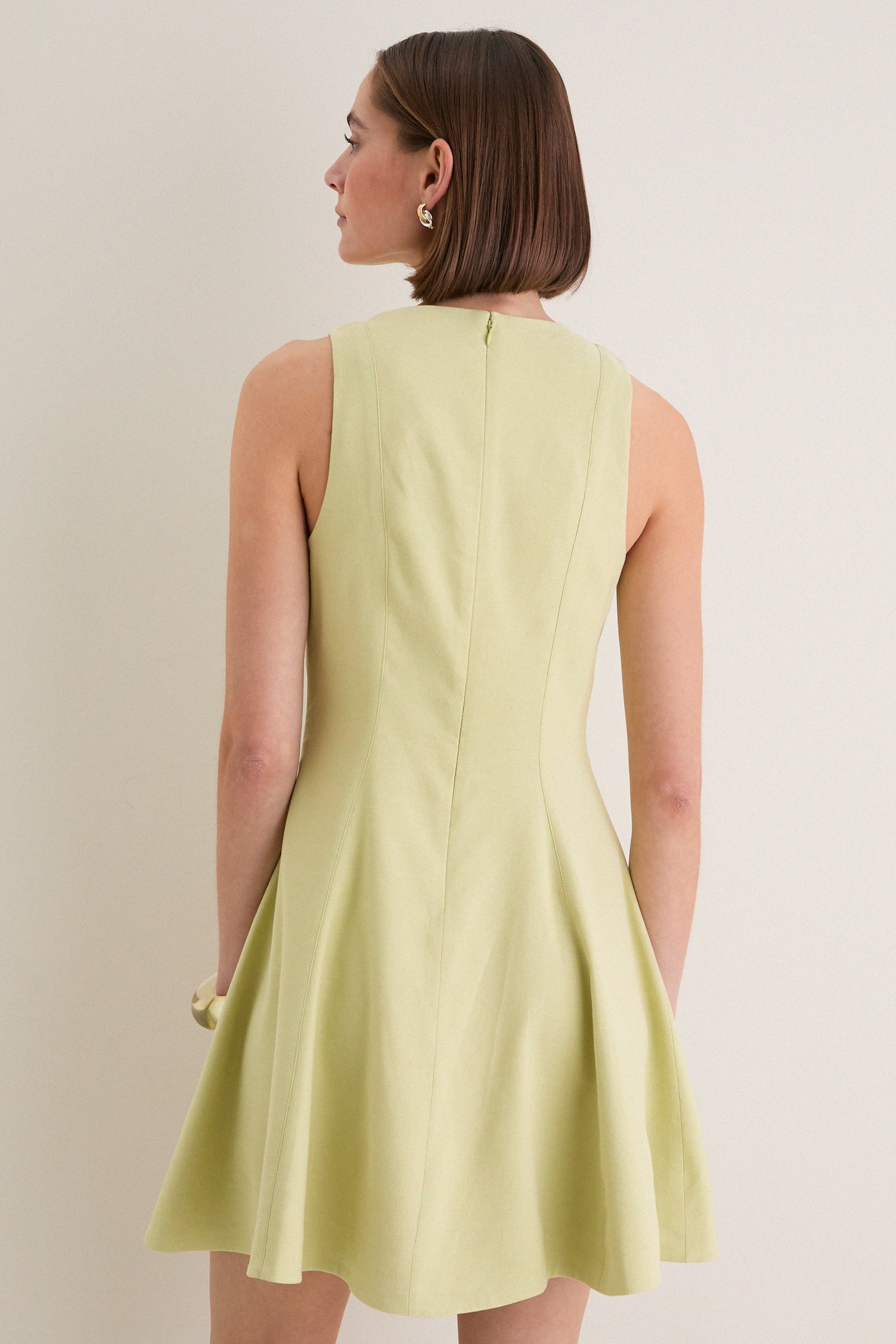Woman in a classic, pale-green sleeveless Pistachio Steiner Dress with a fit-and-flare style, showcasing effortless elegance and fun, high-end fashion.