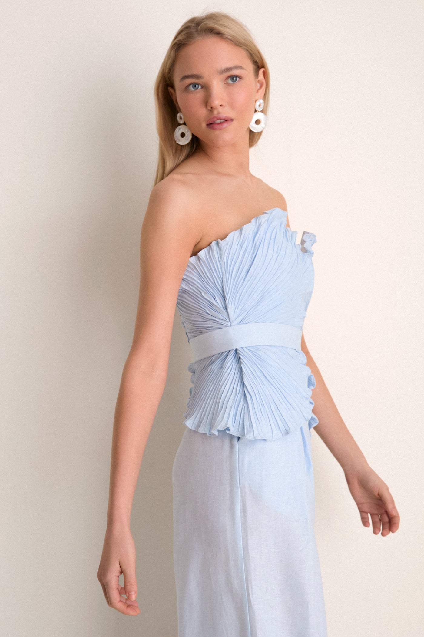 Woman in elegant, strapless Baby Blue De Tres Embellished Top with sweetheart neckline and pleated bodice, capturing effortless, high-end style against a simple backdrop.