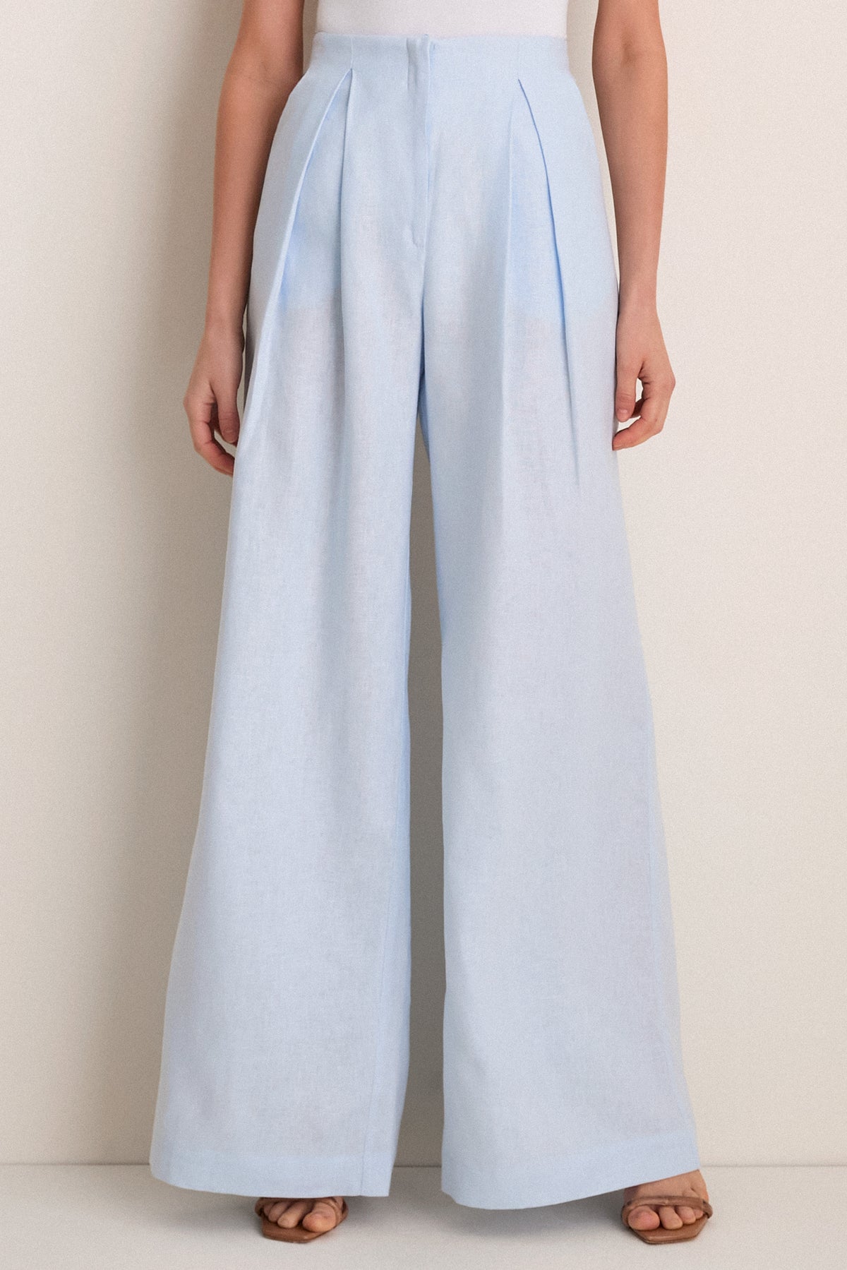 Classic Baby Blue Naces Tu Pants in high-rise, wide-leg silhouette with front pleats, styled with tan sandals. Effortless, high-end look for versatile occasions.