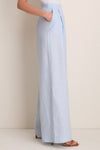 Classic Baby Blue Naces Tu Pants in breathable linen, high-waisted with wide legs and front pleats, paired with strappy tan-brown heeled sandals for an effortless, high-end look.