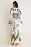Woman in Green Floral Border Que Energia Tunic Dress, showcasing a classic, effortless style with oversized botanical motifs and cream-yellow heeled mules.
