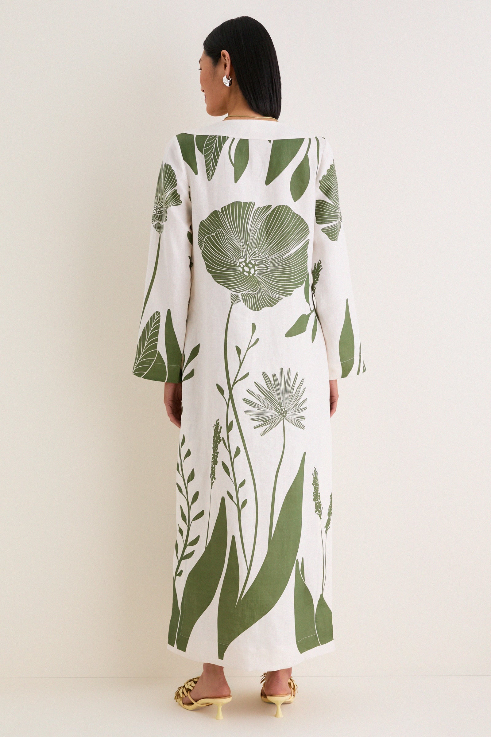 Woman in Green Floral Border Que Energia Tunic Dress, showcasing a classic, effortless style with oversized botanical motifs and cream-yellow heeled mules.