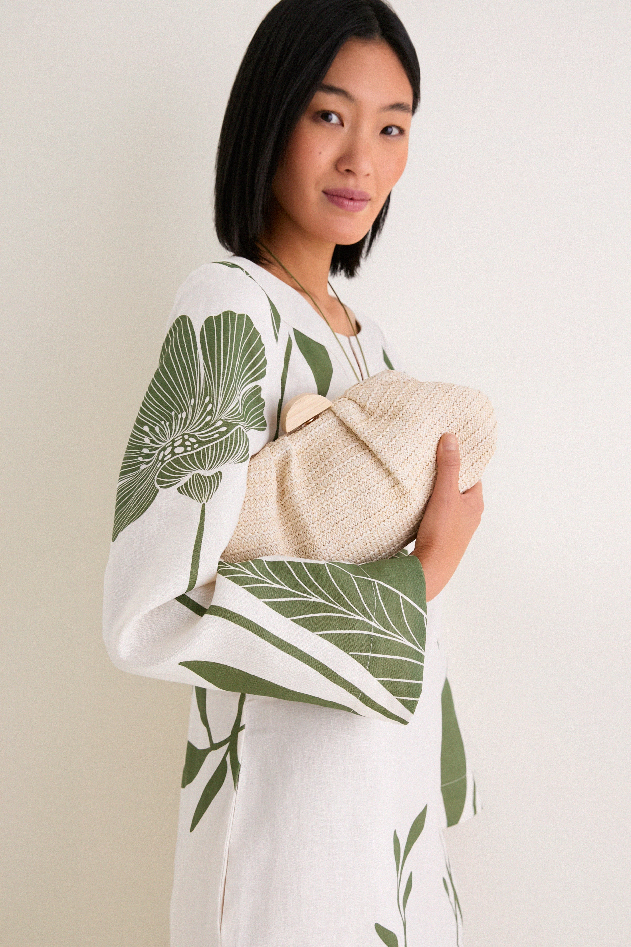 Woman in a classic, effortless Green Floral Border Que Energia Tunic Dress, holding a woven clutch, exemplifying high-end, fun style with relaxed, wide-sleeve design.