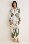 Person wearing the classic Green Floral Border Que Energia Tunic Dress with a relaxed silhouette and V-neckline, holding a woven clutch, paired with effortless yellow heeled sandals.
