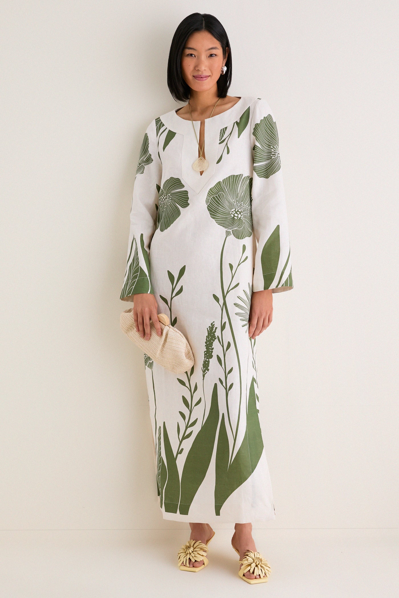 Person wearing the classic Green Floral Border Que Energia Tunic Dress with a relaxed silhouette and V-neckline, holding a woven clutch, paired with effortless yellow heeled sandals.