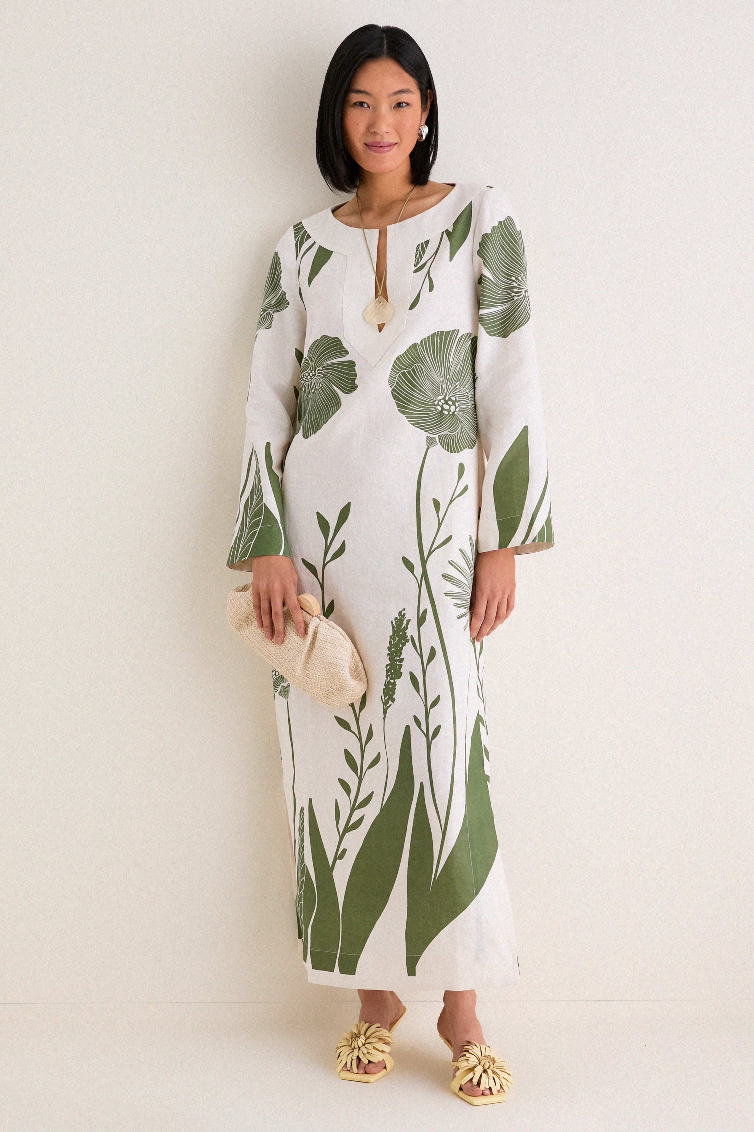 Person wearing the classic Green Floral Border Que Energia Tunic Dress with a relaxed silhouette and V-neckline, holding a woven clutch, paired with effortless yellow heeled sandals.