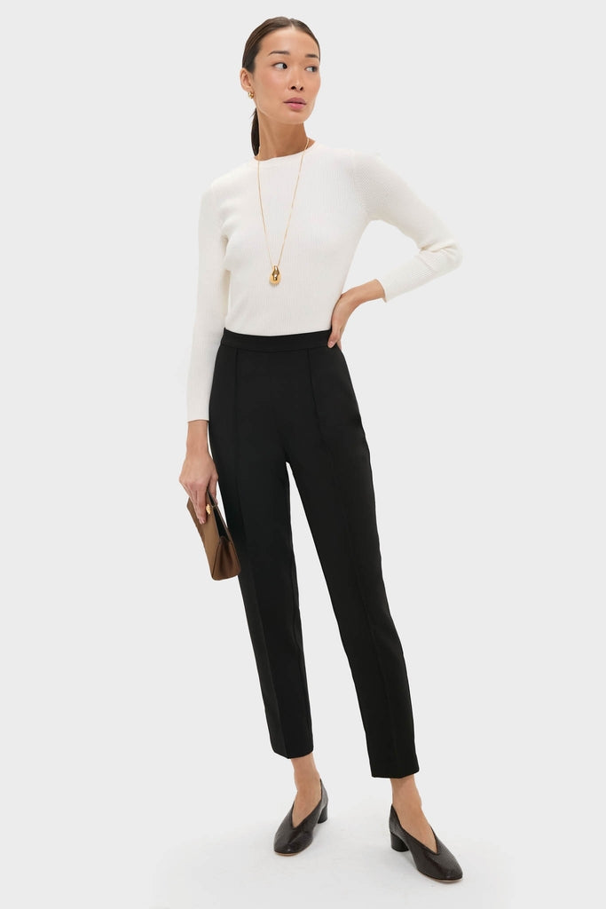 Woman models classic Black Audrey Pants with a sleek fit, paired with an effortless white sweater and fun accessories, capturing a high-end, polished look.