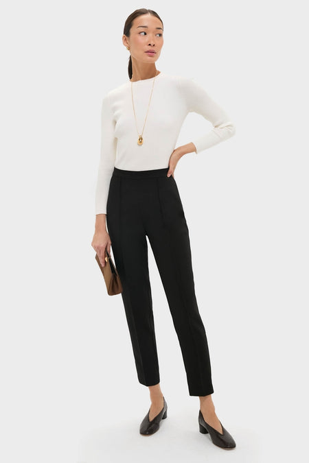Woman models classic Black Audrey Pants with a sleek fit, paired with an effortless white sweater and fun accessories, capturing a high-end, polished look.