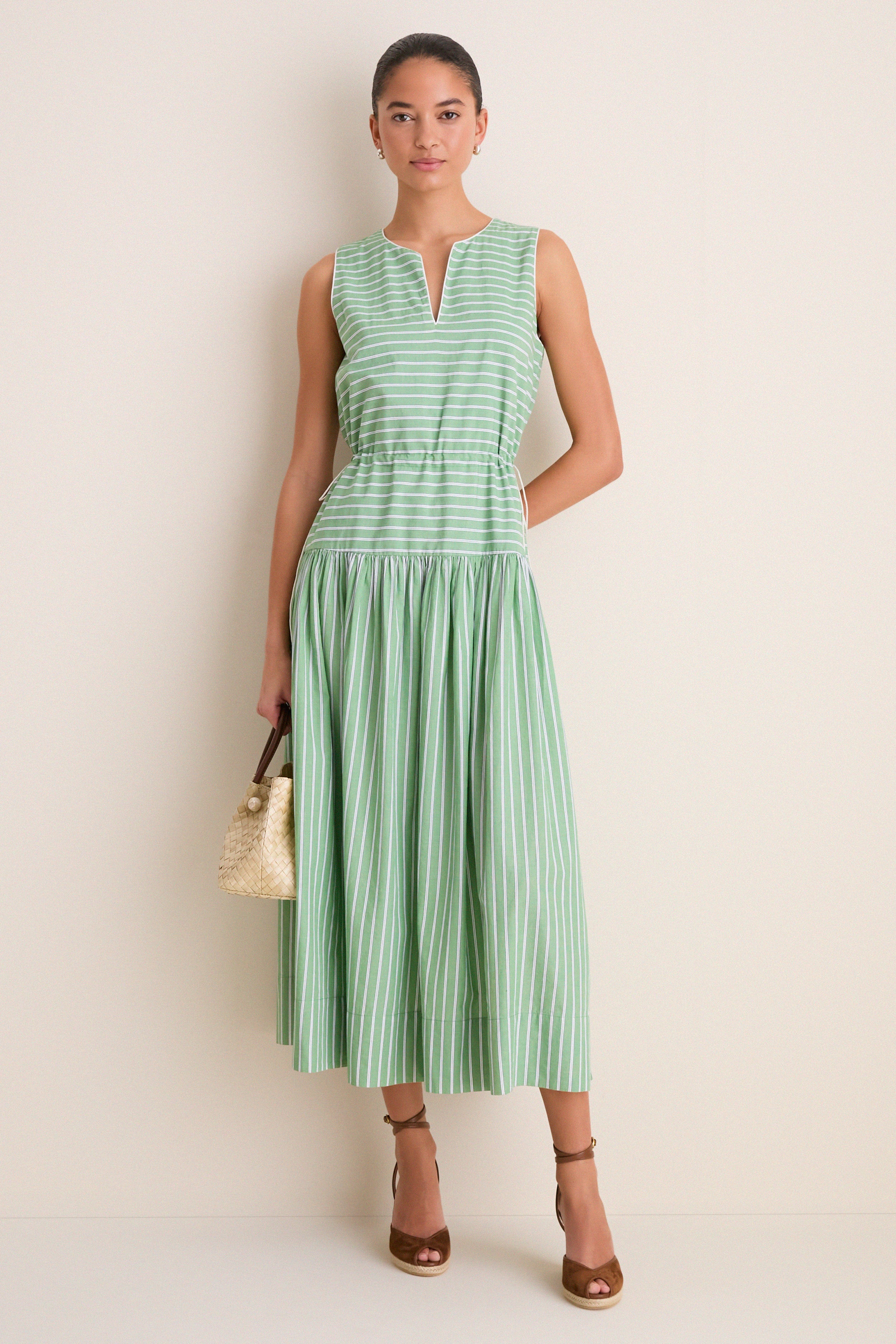 Young woman in a classic sleeveless dress, carrying a woven handbag, wears high-end Chestnut Suede Pasina Wedges, effortlessly blending fun and elevated style.