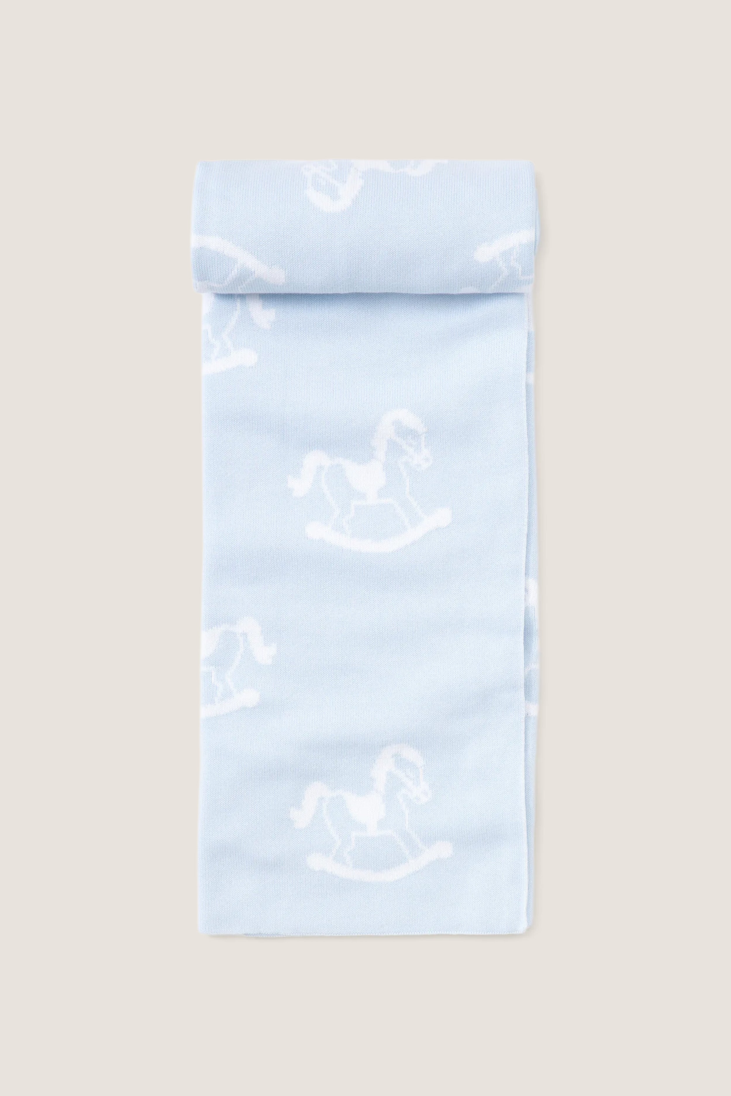 Blue Rocker Knit Blanket, a classic, ultra-soft cotton blanket featuring a playful white rocking-horse pattern on pale blue, perfect for effortless, high-end snuggling with your little one.