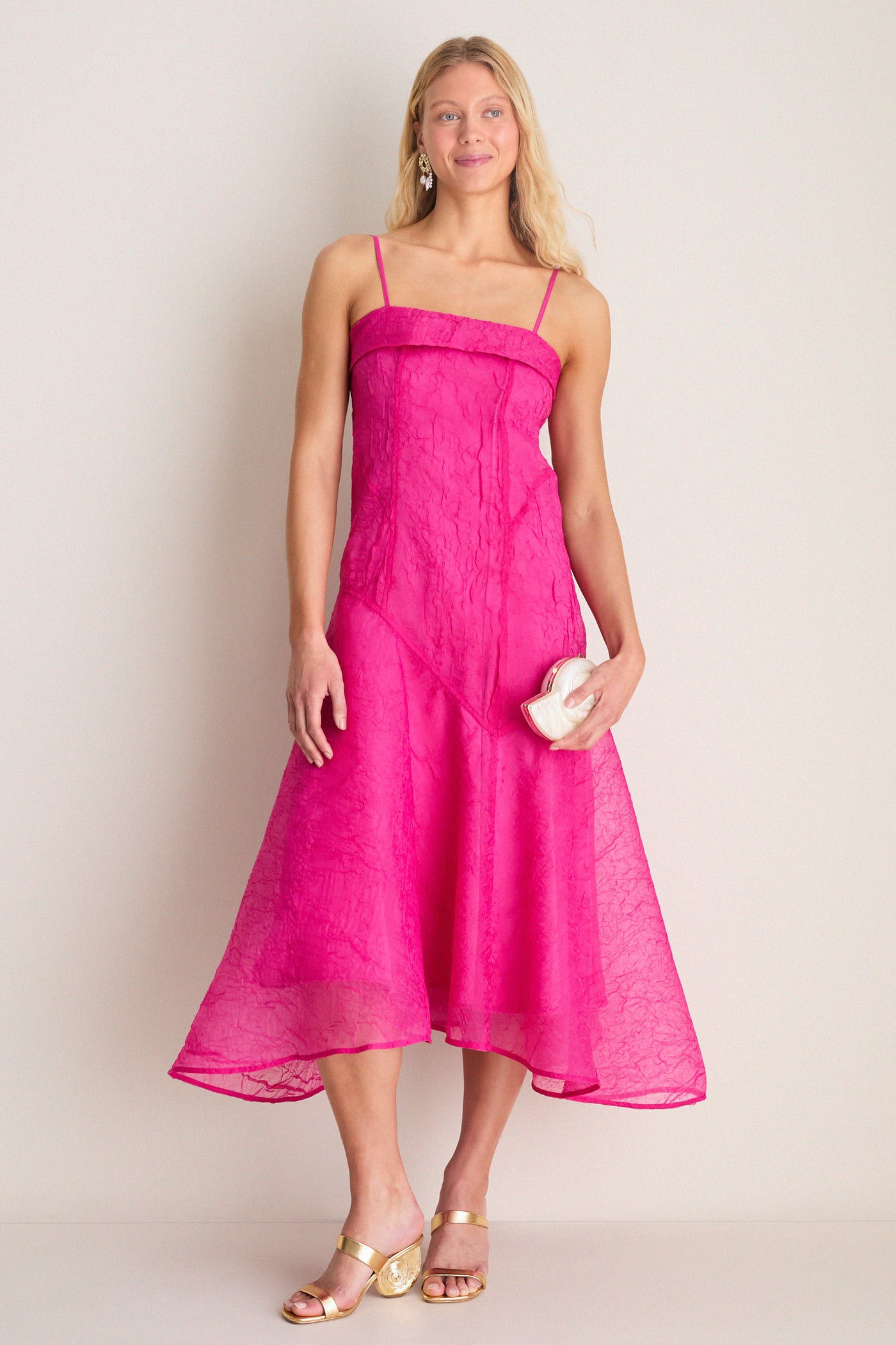 Model in a fuchsia dress showcases classic, high-end Gold Marion Metallic Shell Heels with a sculptural spiral heel, embodying effortless style and fun sophistication.
