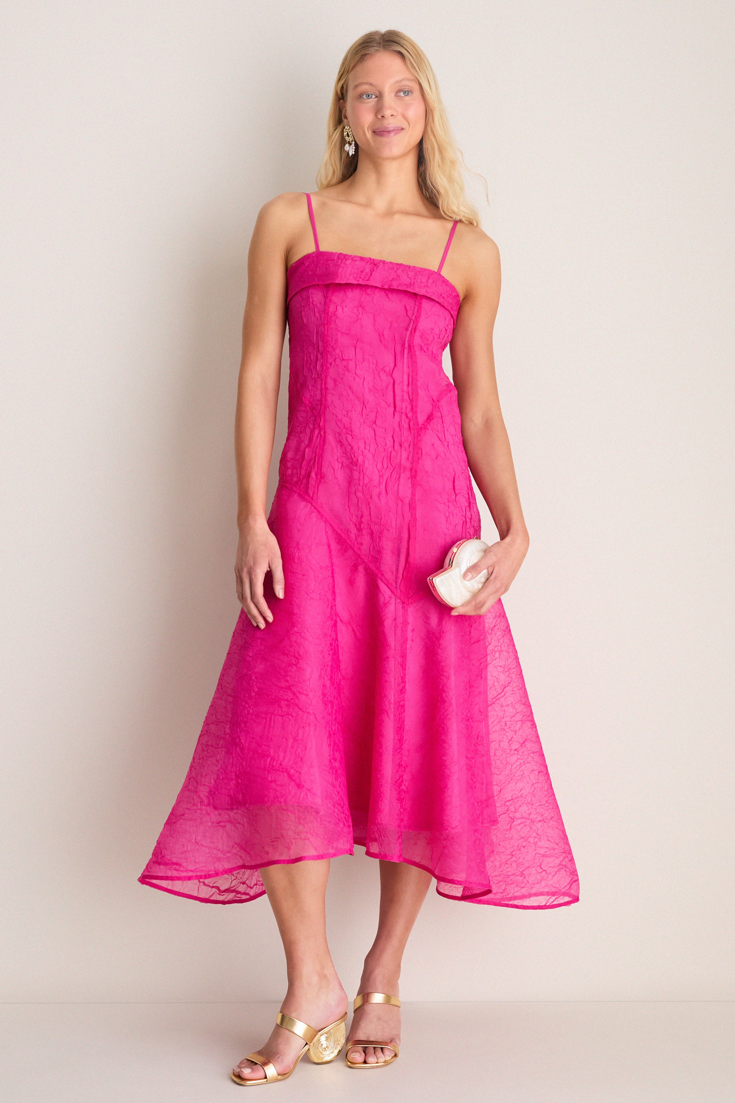 Model in a fuchsia dress showcases classic, high-end Gold Marion Metallic Shell Heels with a sculptural spiral heel, embodying effortless style and fun sophistication.