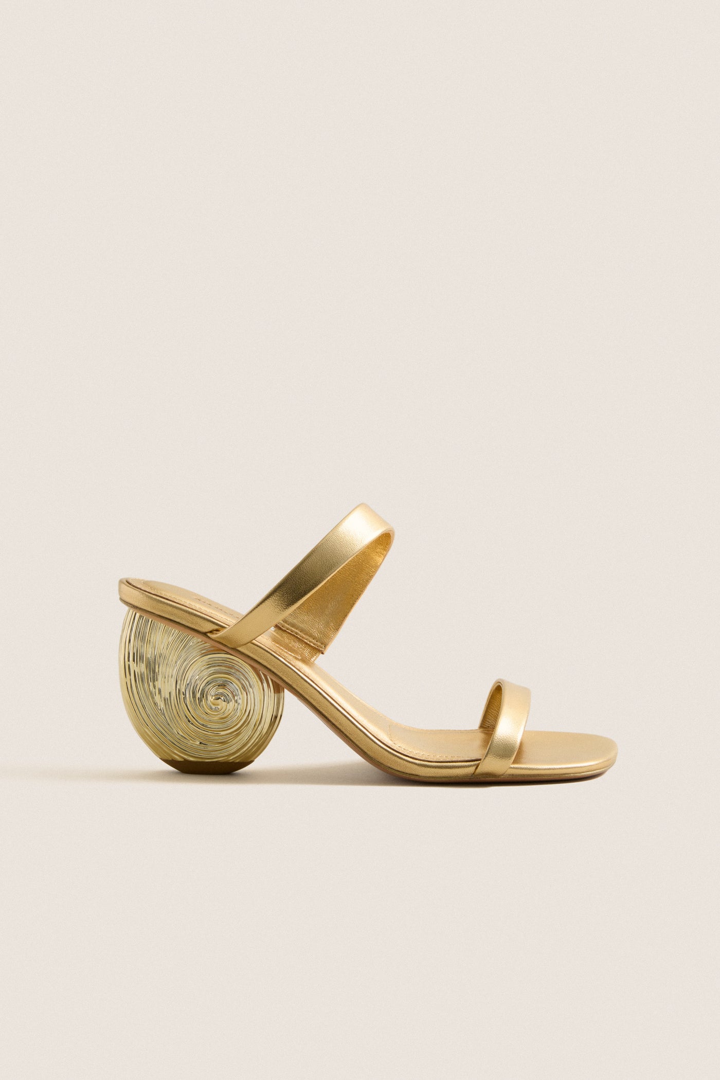 Gold Marion Metallic Shell Heels featuring classic, effortless design; minimalist two-strap upper with fun, high-end spiral shell-inspired sculpted heel, crafted in luxurious gold-tone leather.