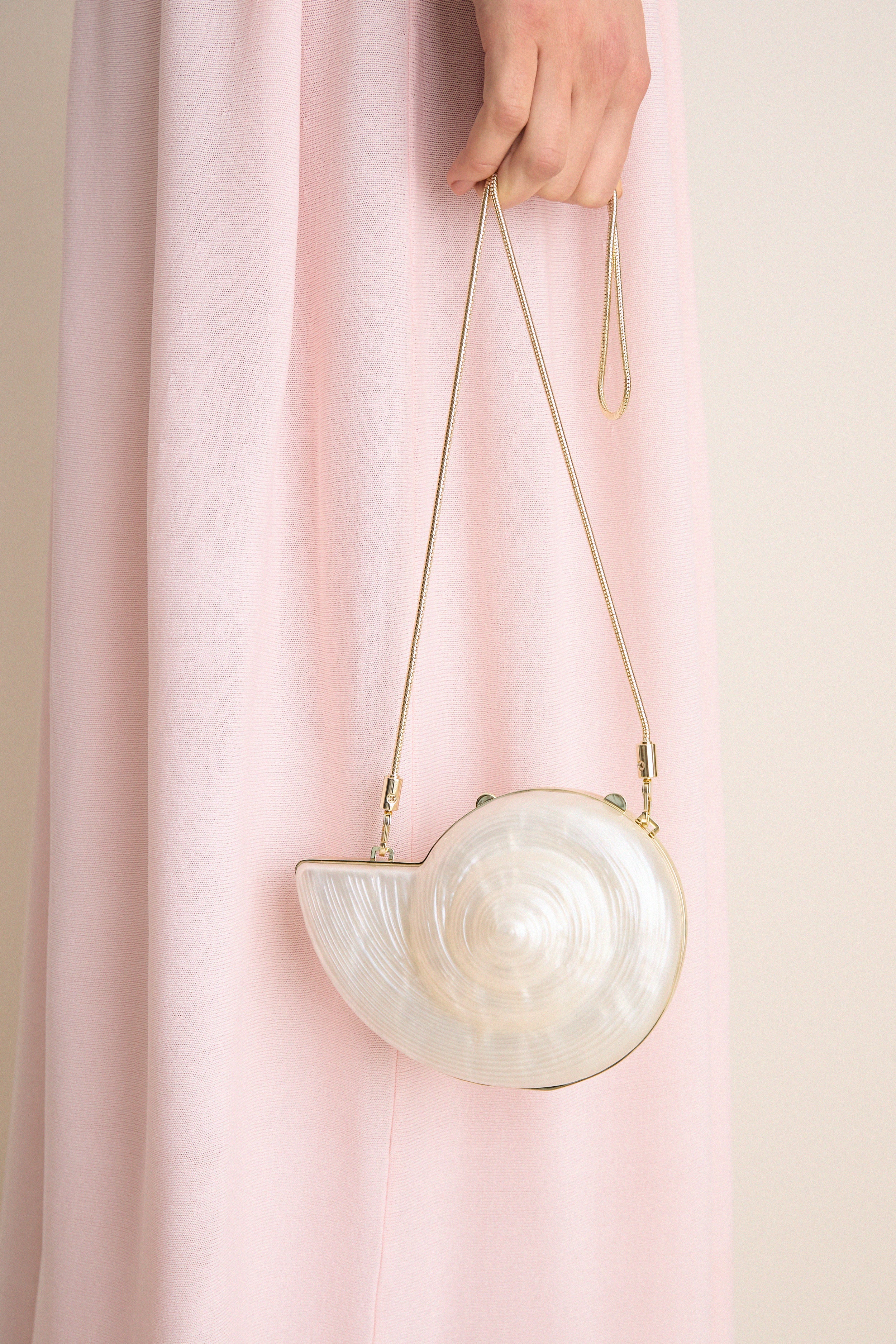 The Pearl Marion Shell Clutch, a classic nautilus-shaped bag with a pearly finish and gold chain, exudes effortless, high-end style for fun occasions.