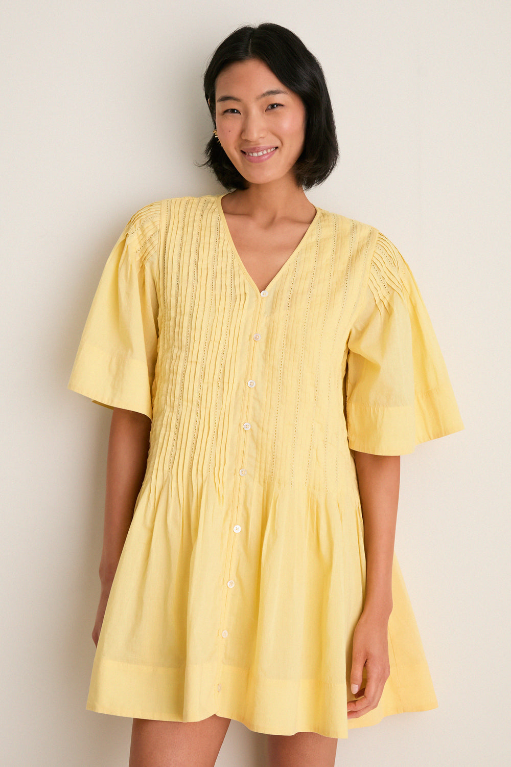 Young woman wearing the classic Yellow Alberte Solid Mini Dress; an effortless, high-end design with pintuck details and buttons, embodying fun, carefree style.