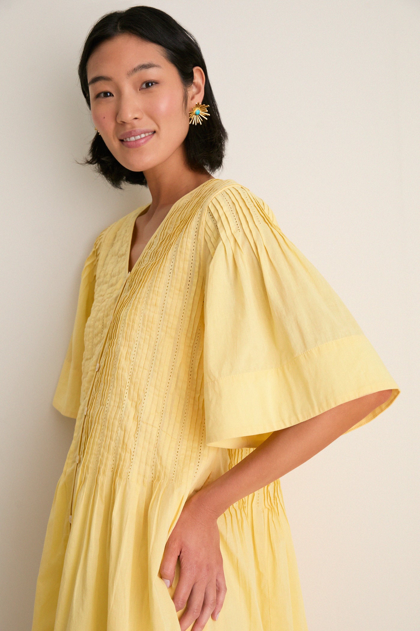 Young woman in a classic, effortless Yellow Alberte Solid Mini Dress, featuring pintuck pleating and elbow-length sleeves, exuding fun and high-end charm.