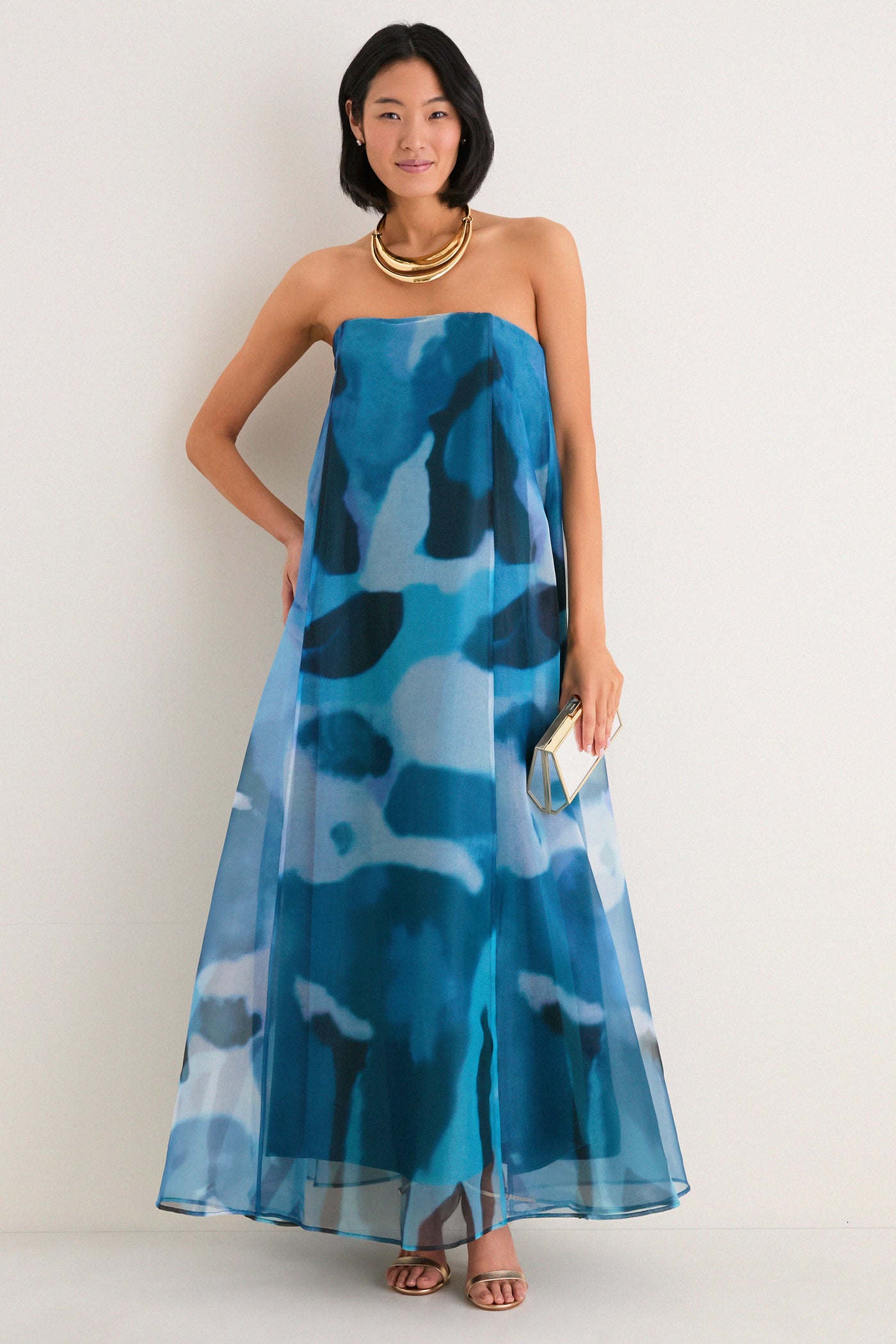 Woman models Blue Haze Allyson Dress, a classic, strapless maxi with corset support, styled effortlessly with gold accessories, embodying high-end, fun elegance.