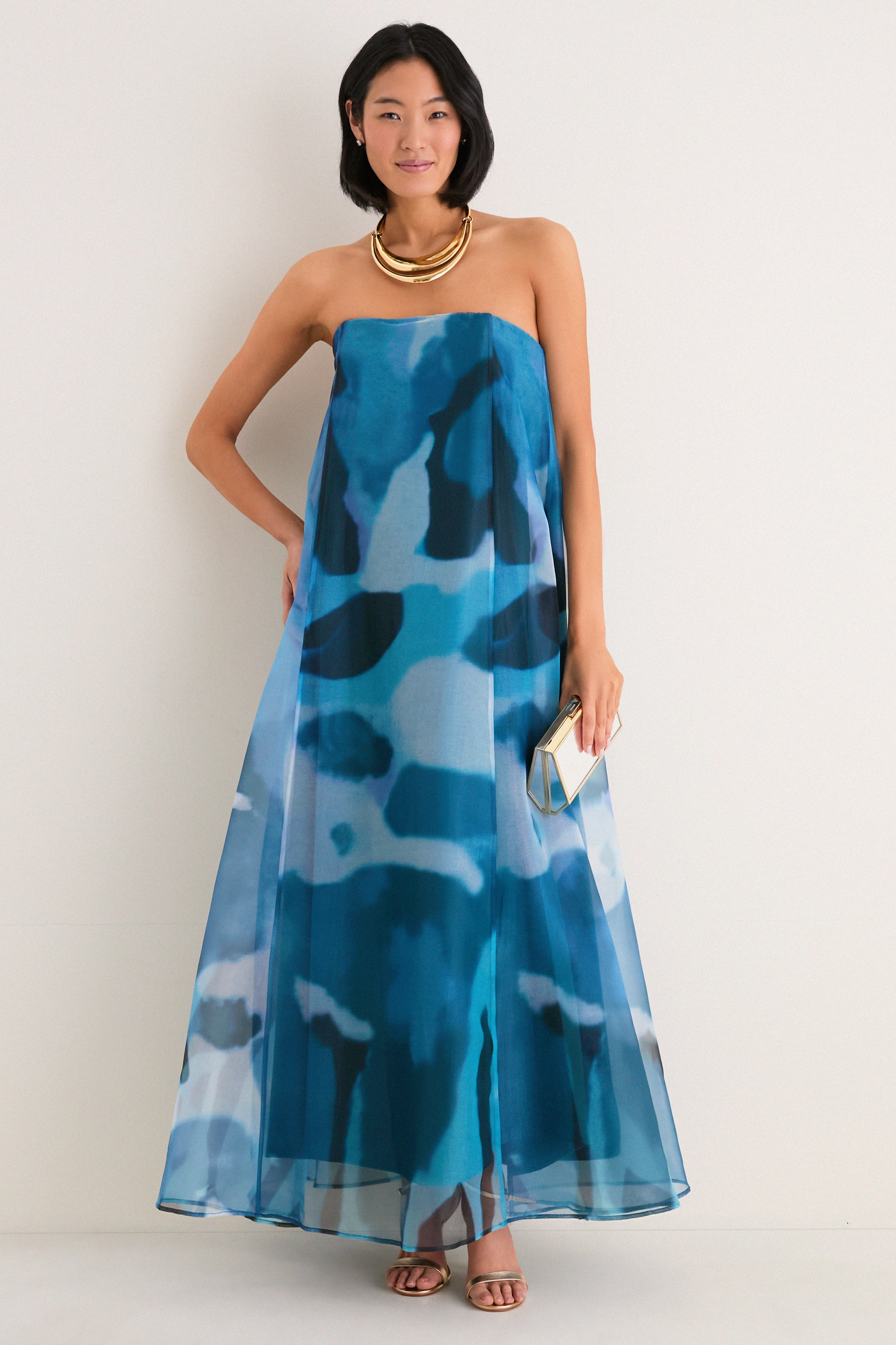Woman models Blue Haze Allyson Dress, a classic, strapless maxi with corset support, styled effortlessly with gold accessories, embodying high-end, fun elegance.