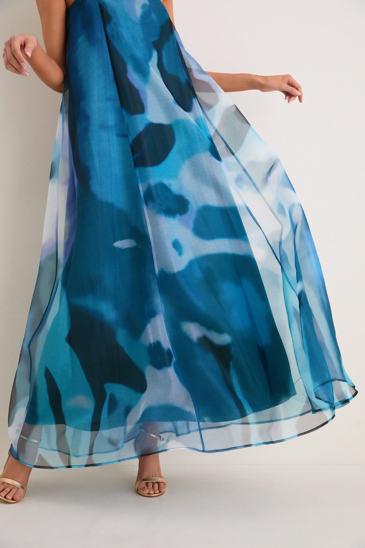 Woman in Blue Haze Allyson Dress, a classic strapless maxi with sheer overlay, paired with gold strappy heels for an effortless, high-end look.