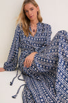 Young woman models the Wave Wonder Nala Maxi Dress, a classic, high-end, navy wrap dress with daisy print, V-neck, voluminous sleeves, and a hand-braided belt for effortless elegance.