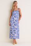 Young woman models the Brocade Azul Tali Maxi Dress, showcasing its classic, effortless design with intricate blue patterns and fun, high-end details like adjustable ties and side slits.
