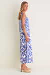 Young woman in Brocade Azul Tali Maxi Dress, a classic white dress with blue paisley-floral print, showcasing effortless style with fun tie-shoulder straps and high-end woven mules.