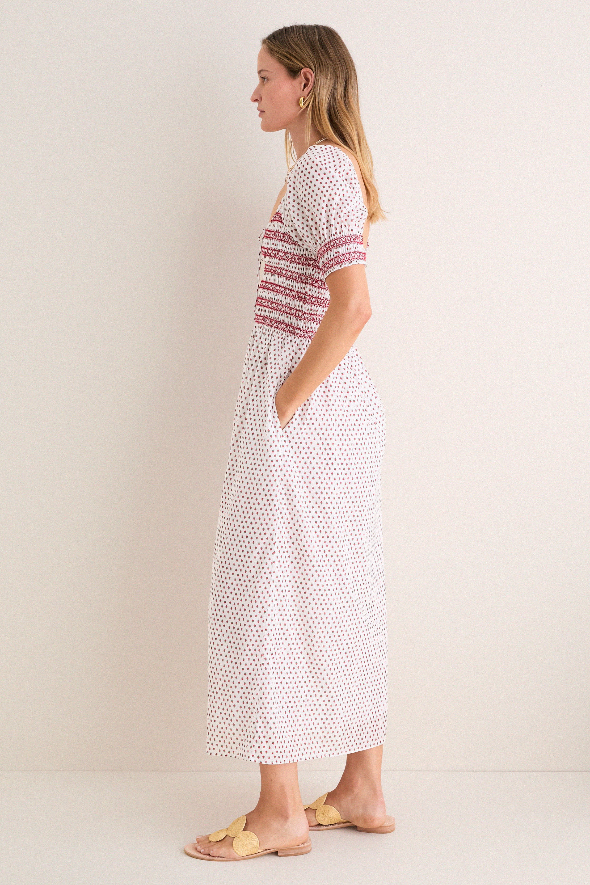 Woman in profile wearing the classic, effortless Poppy Half Drop White Madeline Nap Dress with puffed sleeves, smocked bodice, and fun floral motifs; styled with high-end accessories.