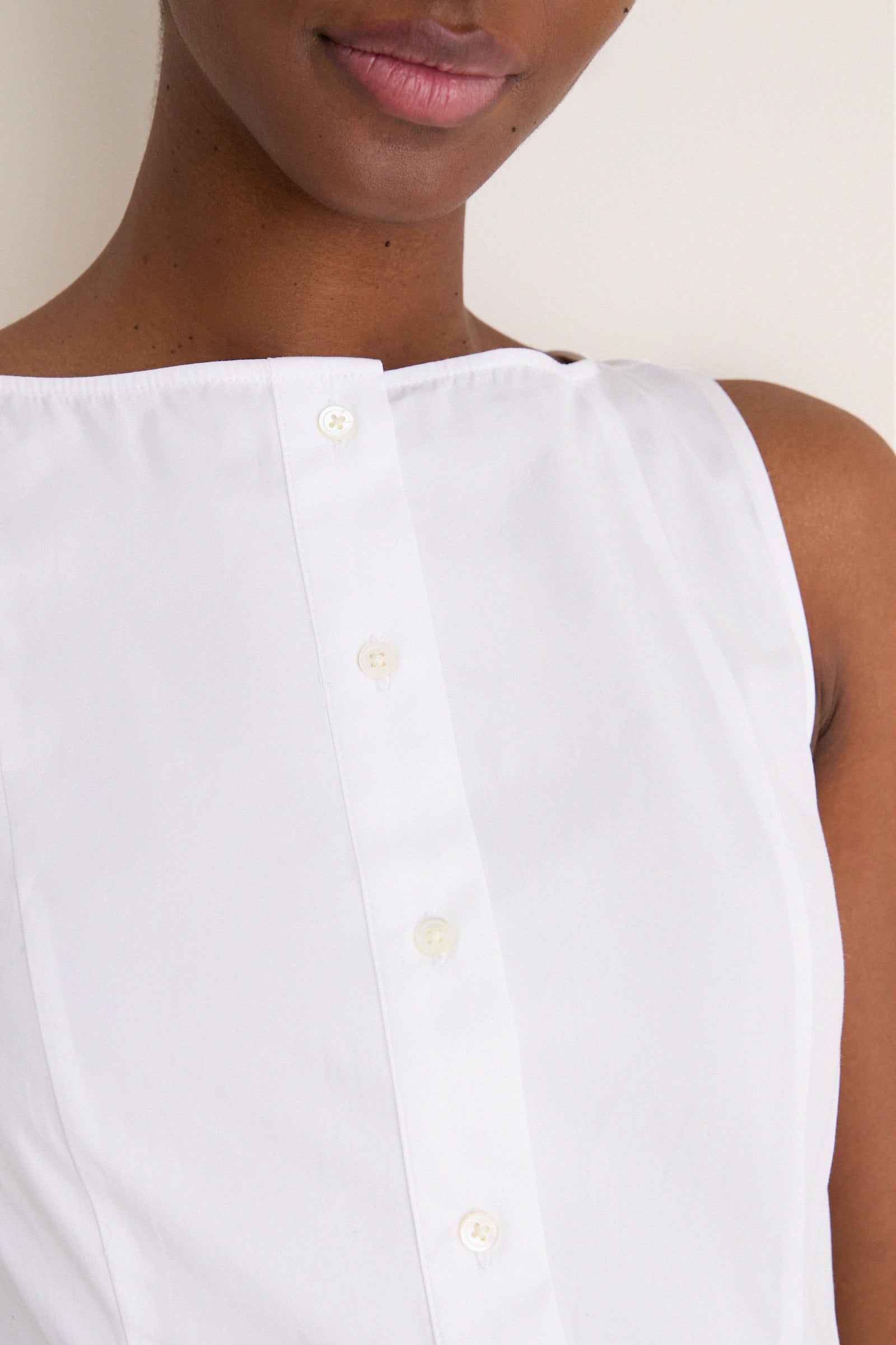 Close-up of a person wearing a classic, sleeveless white cotton boat neck dress, showcasing its effortless, high-end design with a fun, relaxed fit.