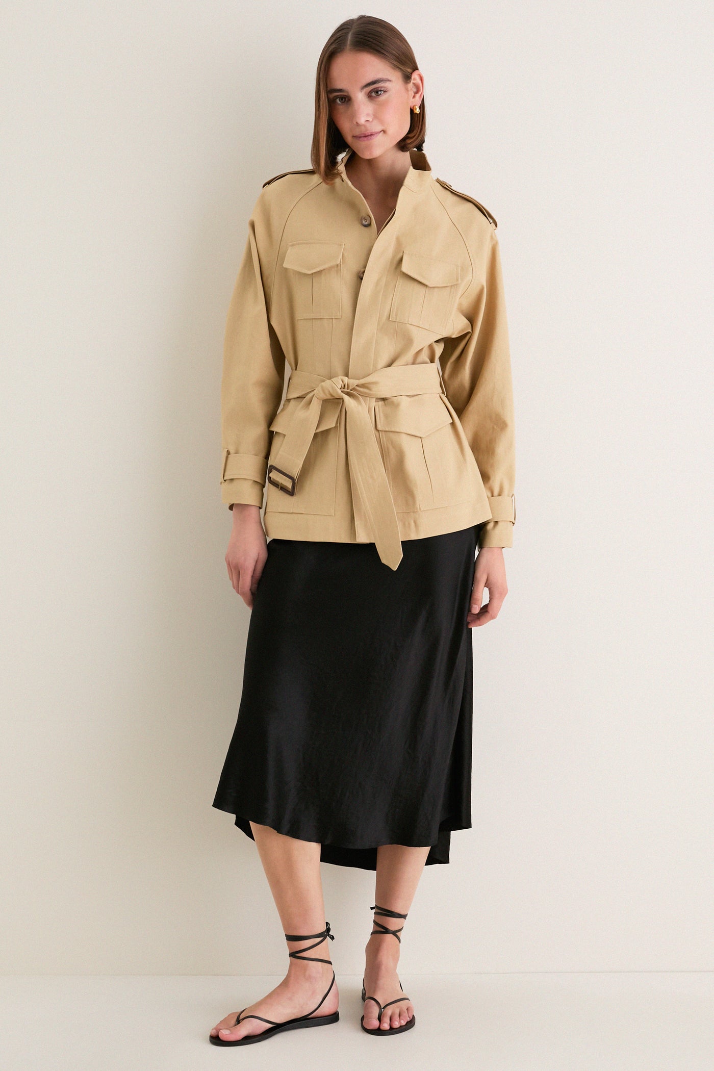 Model in a classic Camel Cotton Field Jacket, showcasing effortless style with flap pockets and a self-tie belt, paired with a black slip skirt and sandals.