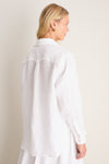 Woman wearing a classic, oversized white linen button-down with gold hoop earrings, embodying effortless, high-end style. The shirt features a relaxed fit and signature details.
