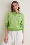 Young woman models a Parakeet Green Island Fleece Knit Polo, showcasing its classic, effortless style with relaxed fit and iconic embroidered logo, paired with white linen trousers.